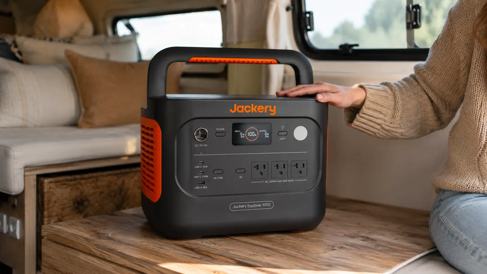 Jackery Explorer 1000 v2 portable power station sitting on a weathered wooden picnic table at a forested campsite in the early morning